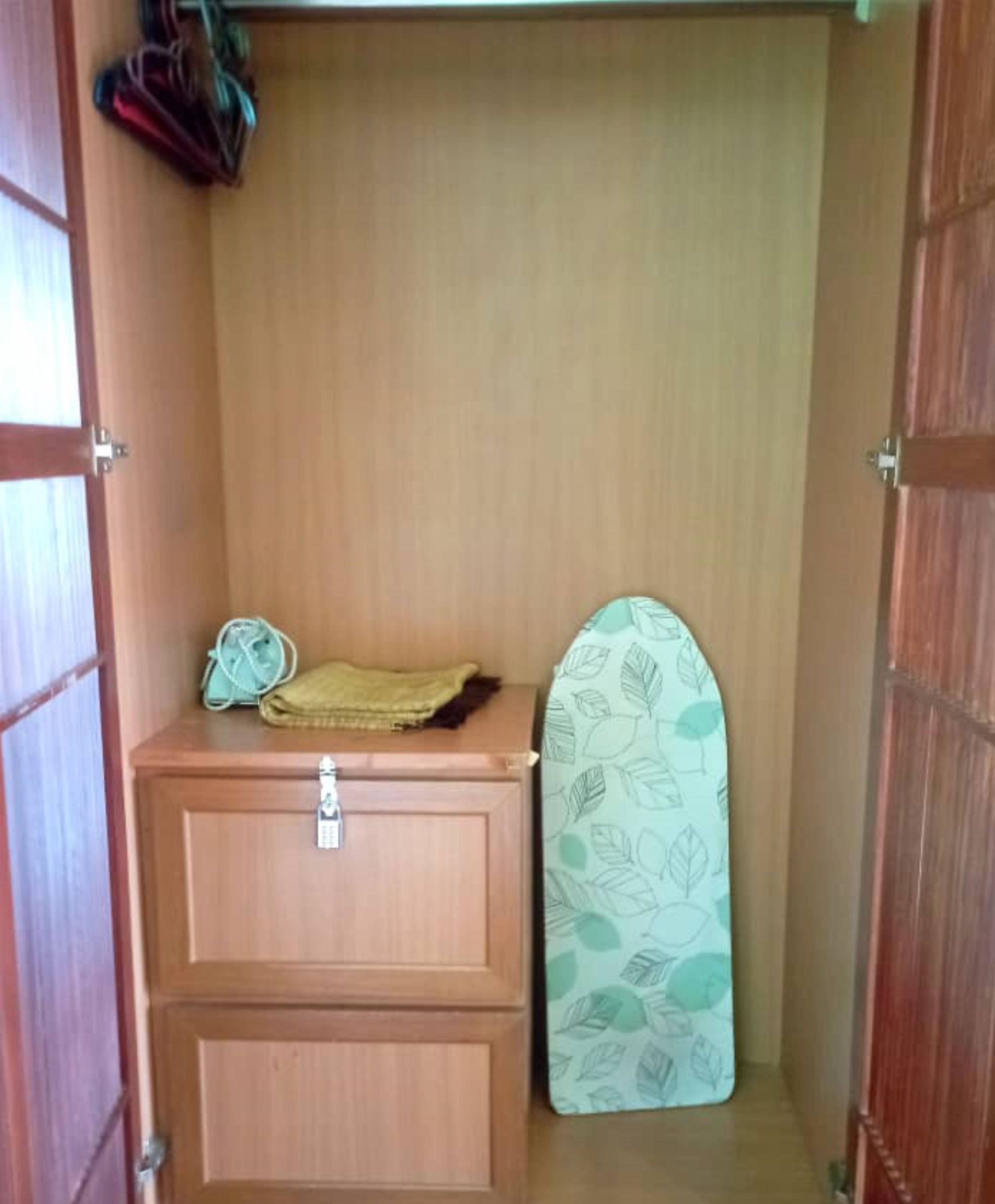 Un pequeño mueble de madera con cerradura, una toalla doblada y una tabla de planchar estampada.