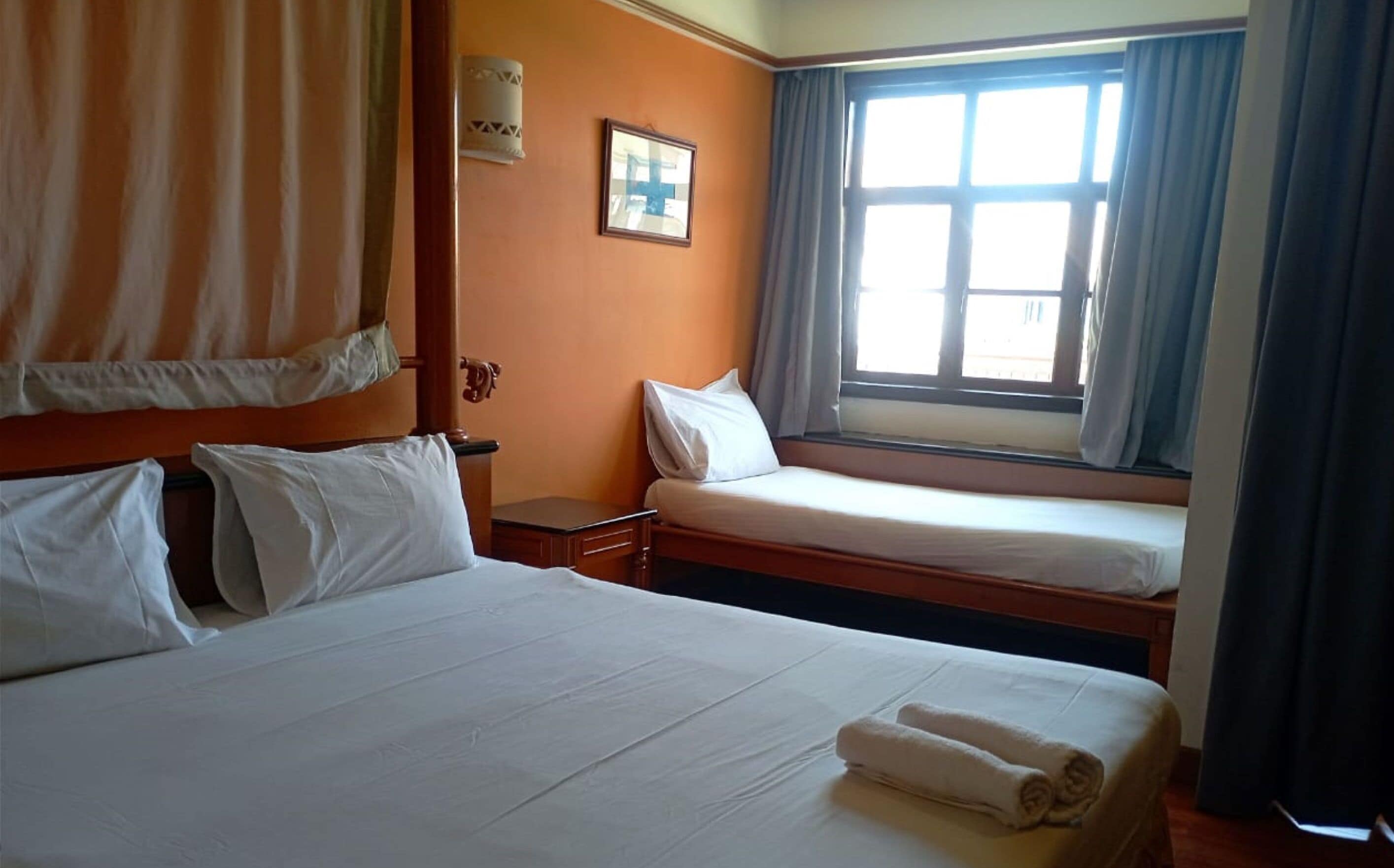 Een hotelkamer met twee bedden, een raam met gordijnen, een nachtkastje en een wandlamp.