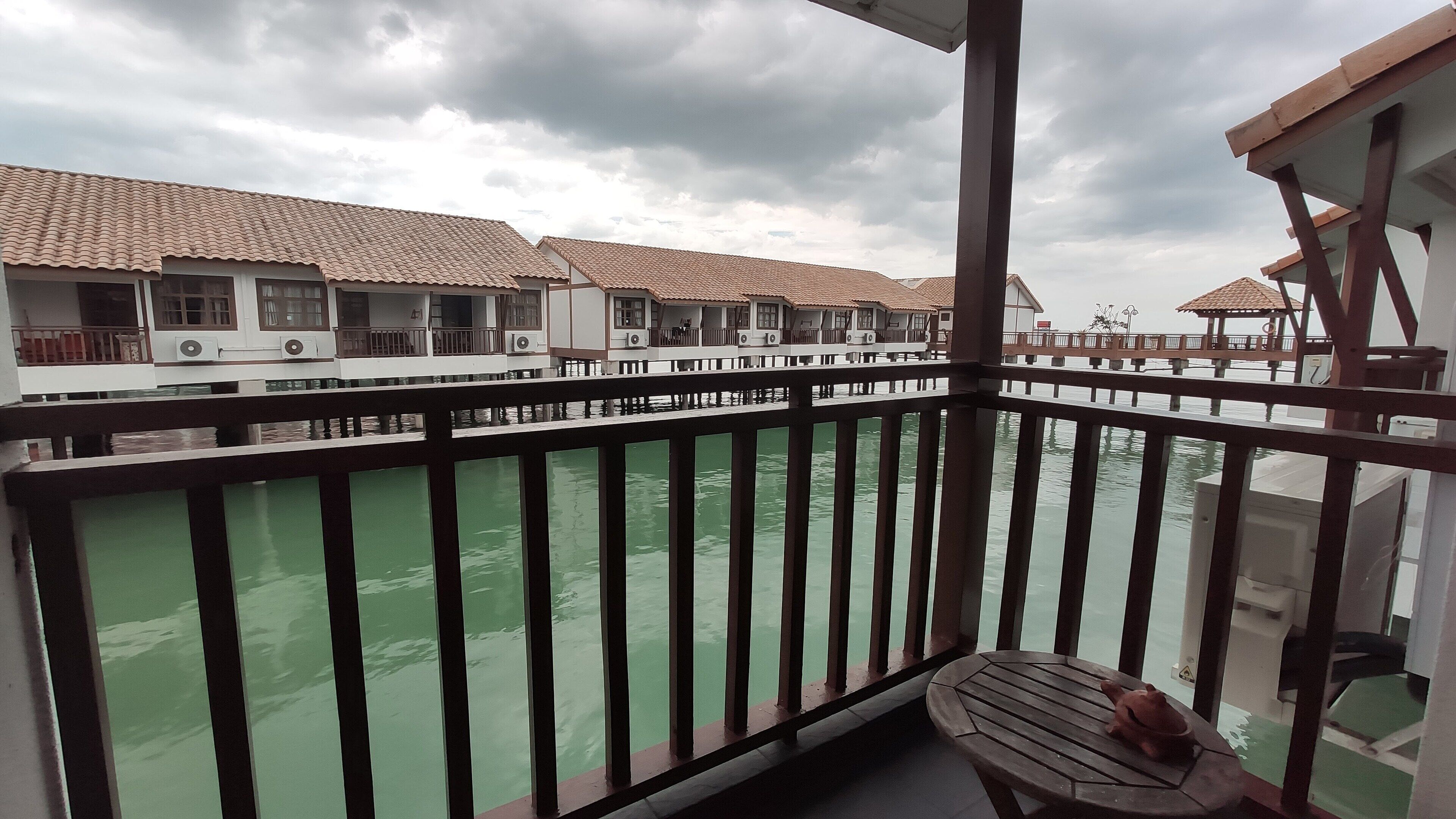 A balcony with a view of overwater bungalows and a wooden chair.