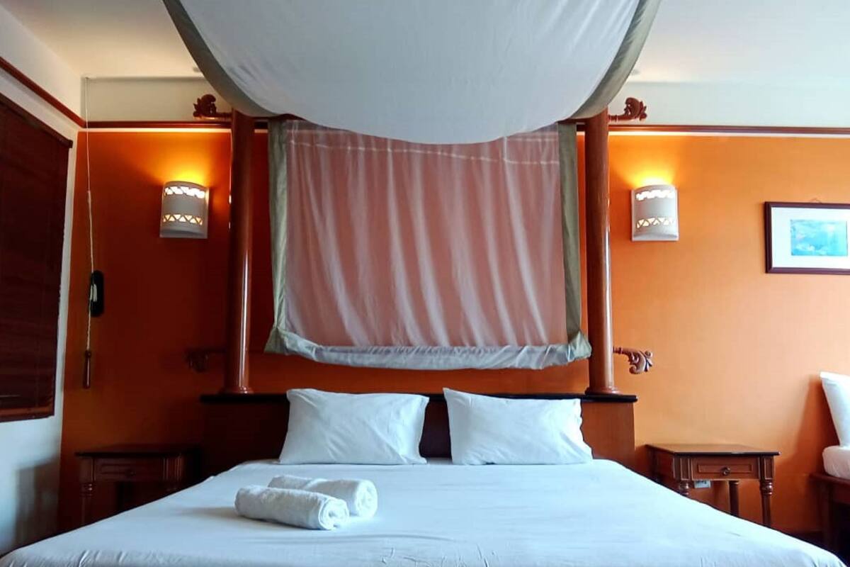 Quarto de hotel com cama de dossel, duas mesas de cabeceira e uma cadeira.