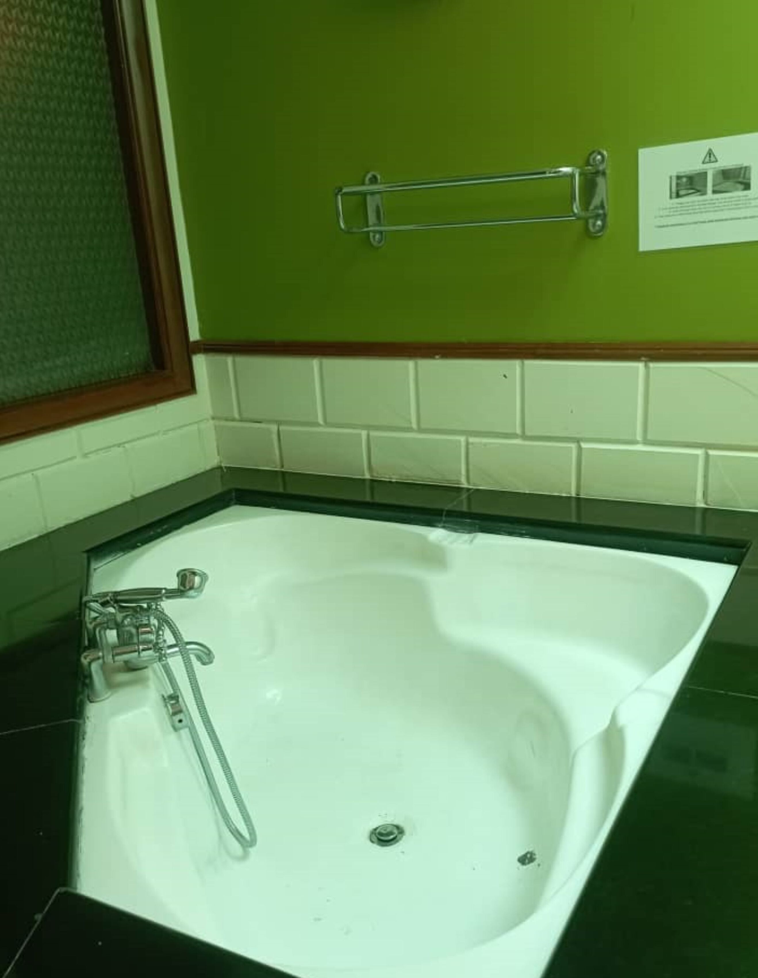 A bathroom with a white bathtub, green walls, and a black countertop.