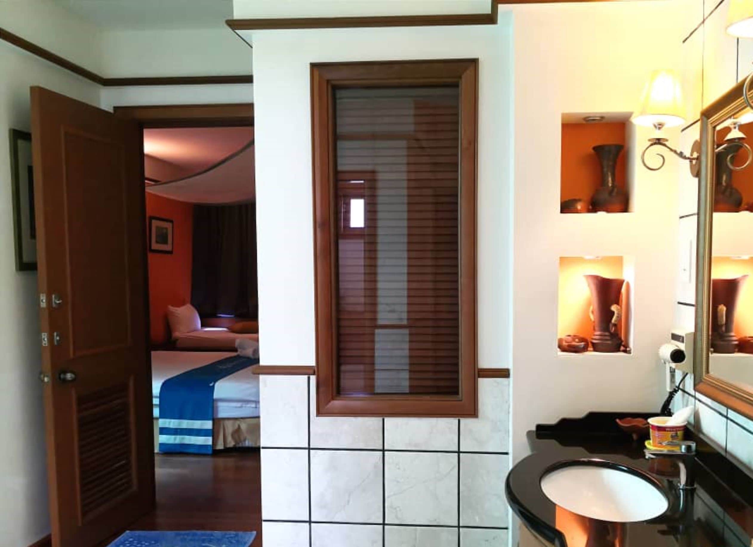 A hotel room with a bed, a bathroom with a sink and mirror, and a window with blinds.
