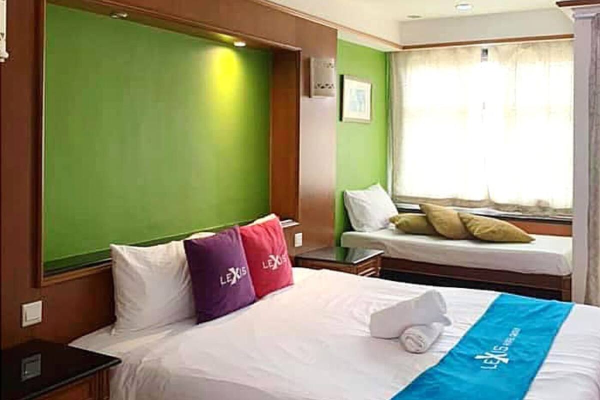 Quarto de hotel com uma cama grande, uma cama menor, paredes verdes e uma janela com cortinas.