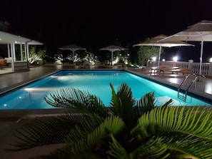 Piscina com espreguiçadeiras e guarda-sóis, cercada por um alpendre coberto.