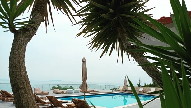 A poolside area with lounge chairs, a covered umbrella, and a view of the sea. - Hotel Relax Dhermi (Himarë)