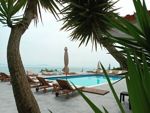 A poolside area with lounge chairs, a covered umbrella, and a view of the sea. - Hotel Relax Dhermi (Himarë)
