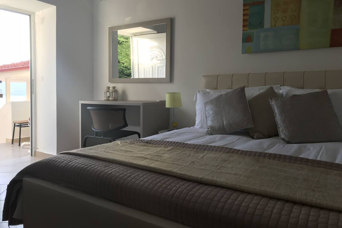 A bedroom with a bed, a desk, a chair, a lamp, and a painting on the wall.