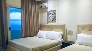 A hotel room with a bed, a nightstand, a lamp, a decorative wall piece, and a view of the sea through a window with curtains. - Hotel Relax Dhermi (Himarë)