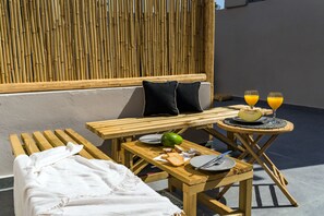 A wooden table set with plates, cutlery, a bowl, and glasses of orange juice, accompanied by a bench and a white towel. - Echo Suites (Santorini)
