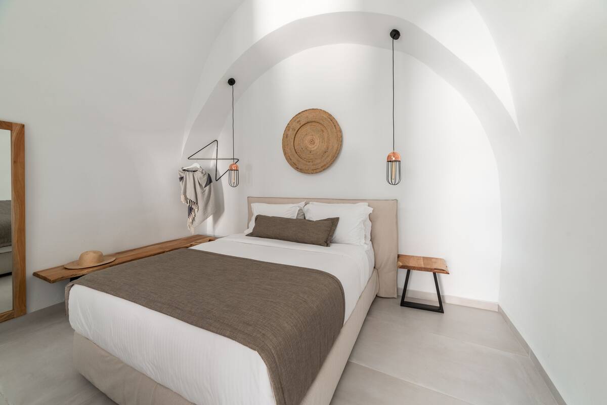 A modern bedroom with a large bed, a wooden bench, a hanging light fixture, and a round wooden wall art piece.