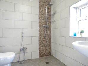 A bathroom with white tiles, a shower with a mosaic wall, a toilet, and a sink with a window view.