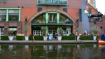 A brick building with a green archway labeled "PITCHER & PIANO AT BRINDLEY PLACE" and outdoor seating with potted plants.