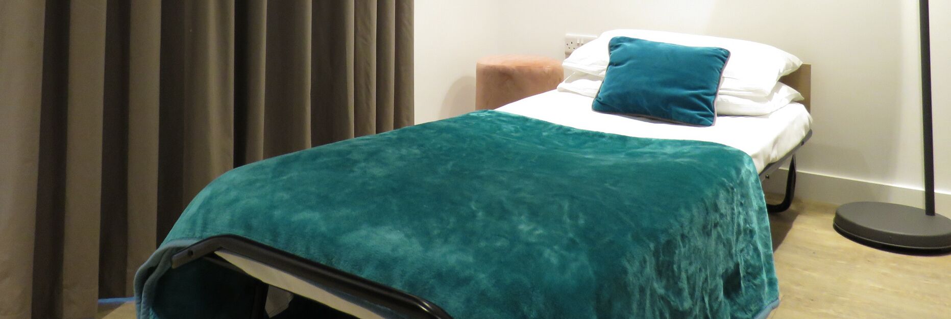 A small, neatly made bed with a teal blanket and a single blue pillow.