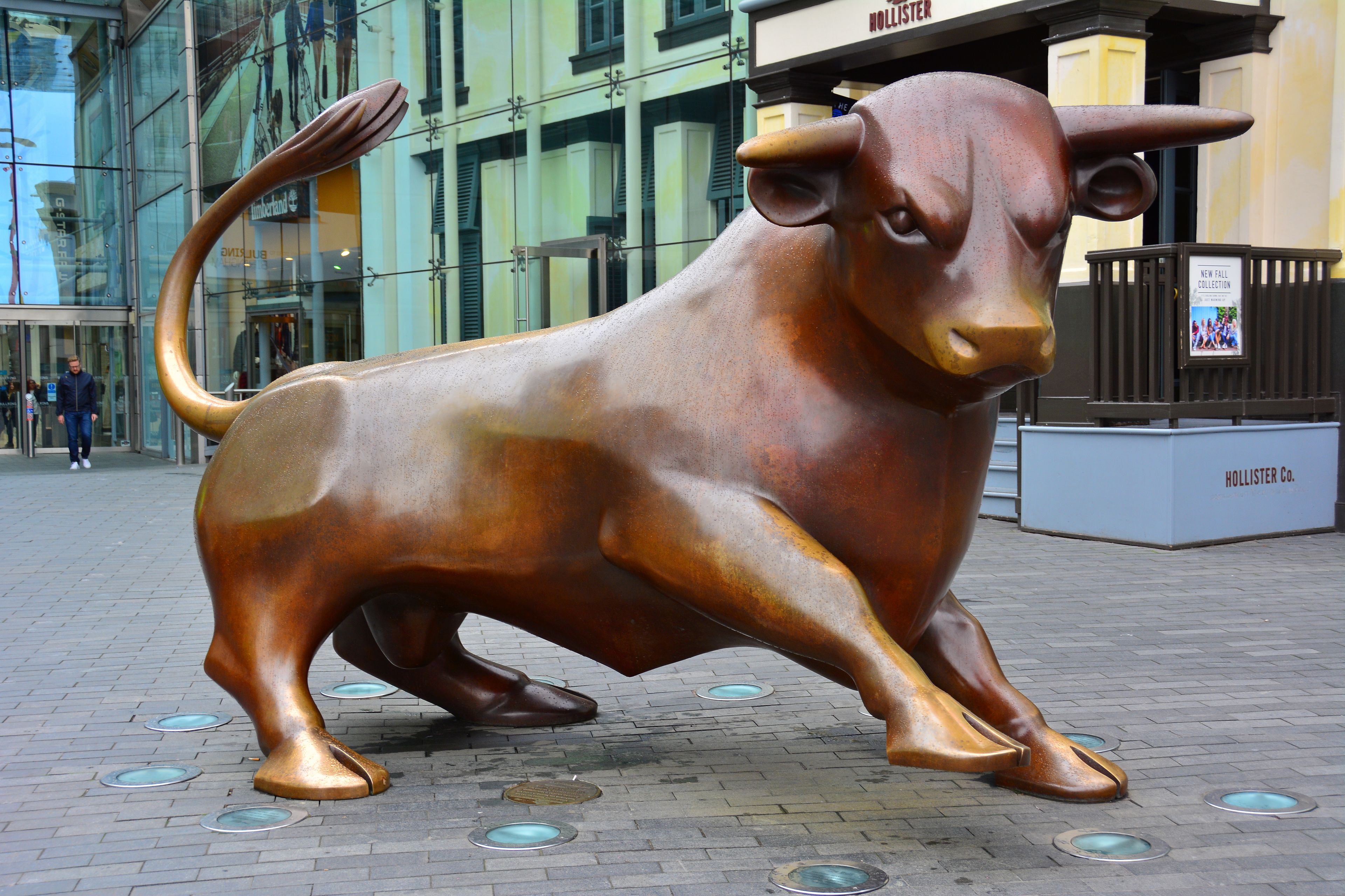 A bronze bull sculpture on a paved area with a building in the background.