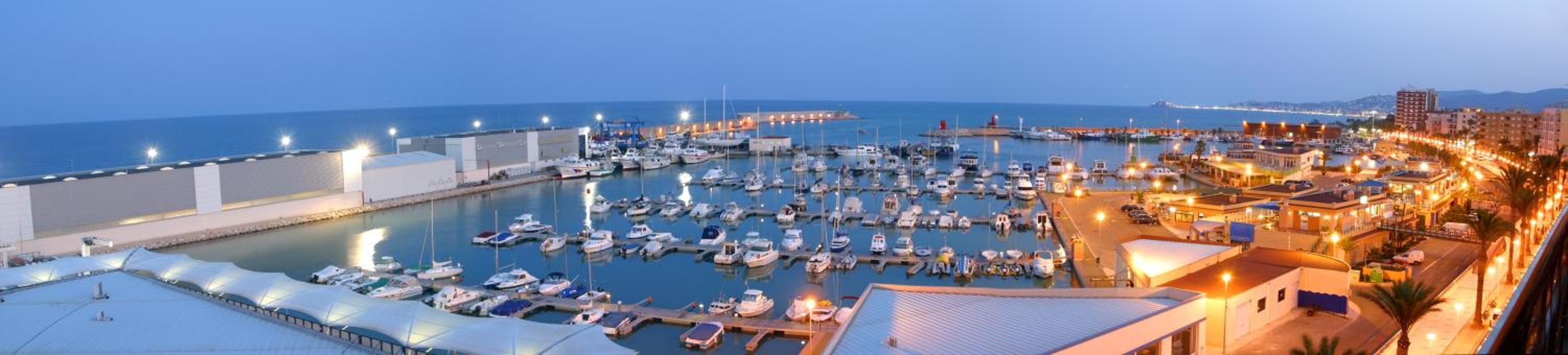 A marina with boats docked, a waterfront promenade, and buildings along the shore.