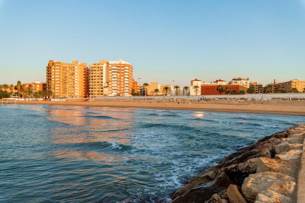 A coastal cityscape with a beach, rocky shoreline, and high-rise buildings.