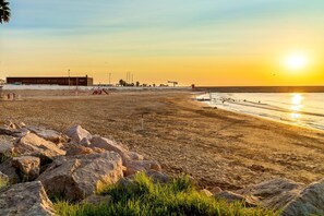 A beach with a building in the background, a clear sky, and the sun setting over the water. - Las Cebras Apartamentos Turísticos (Benicarlo)