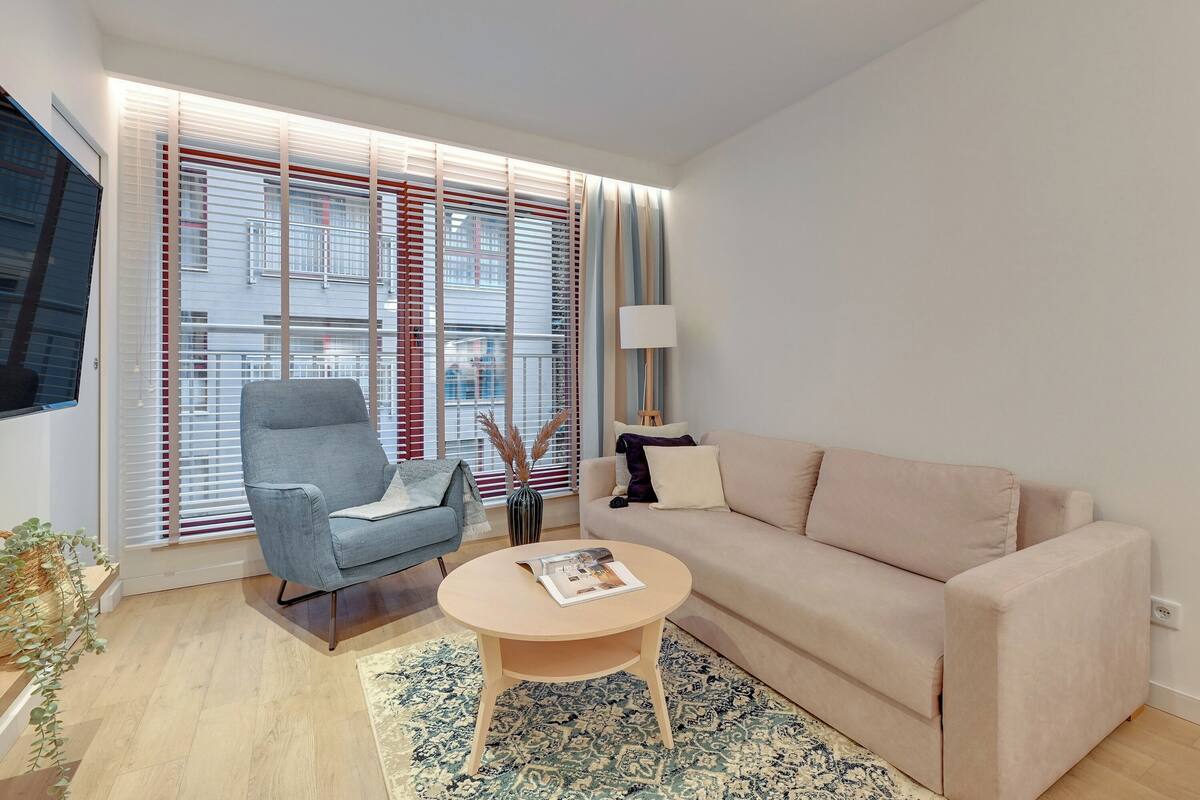 A modern living room with a sofa, armchair, coffee table, and a large window with blinds.