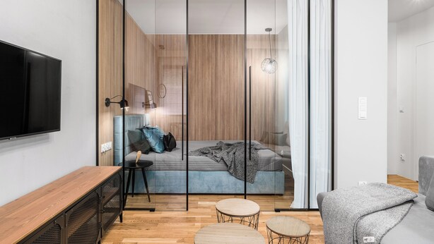 A modern bedroom with a sliding glass door, a bed, a TV, and a wooden floor.