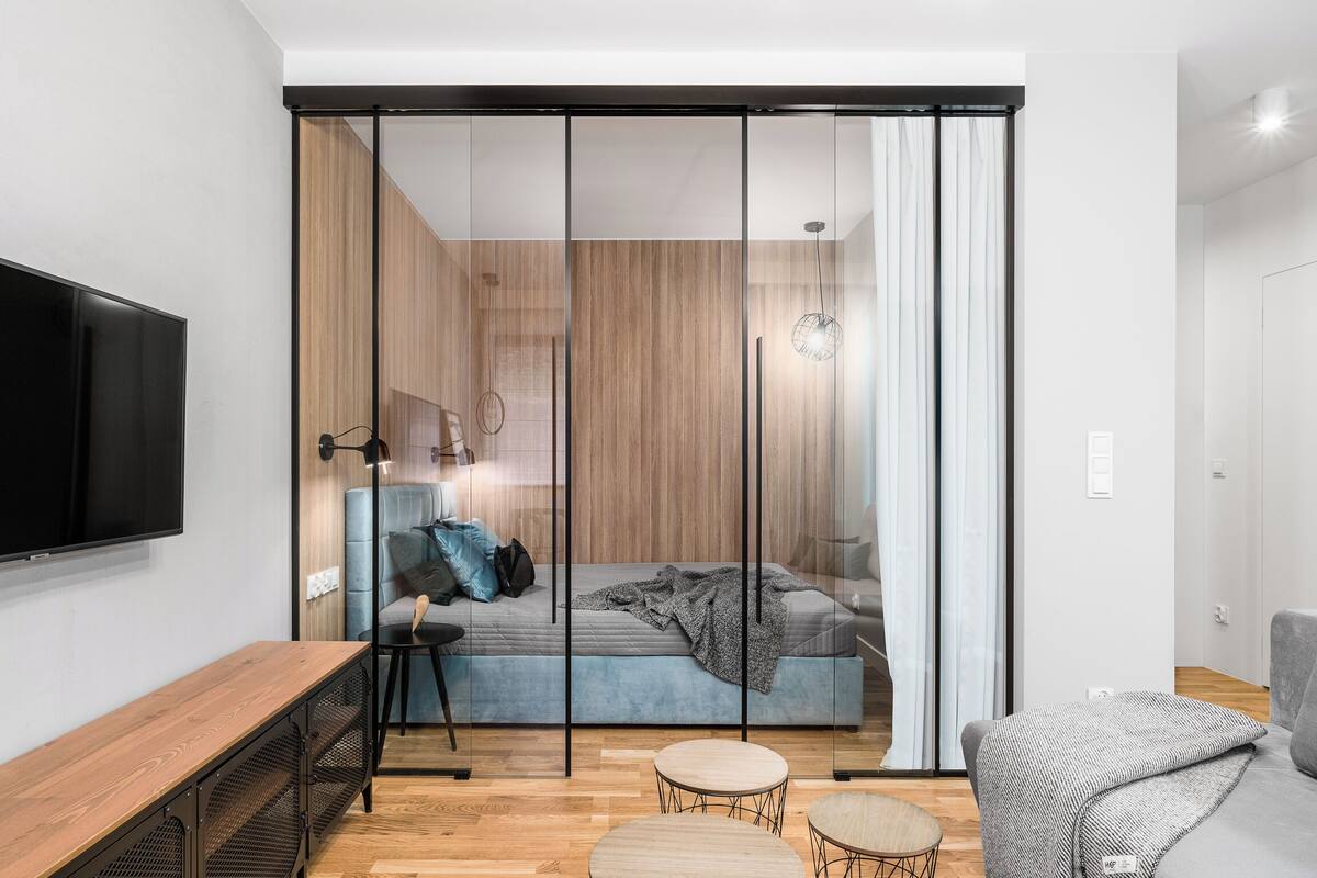 A modern bedroom with a sliding glass door, a bed, a TV, and a wooden floor.