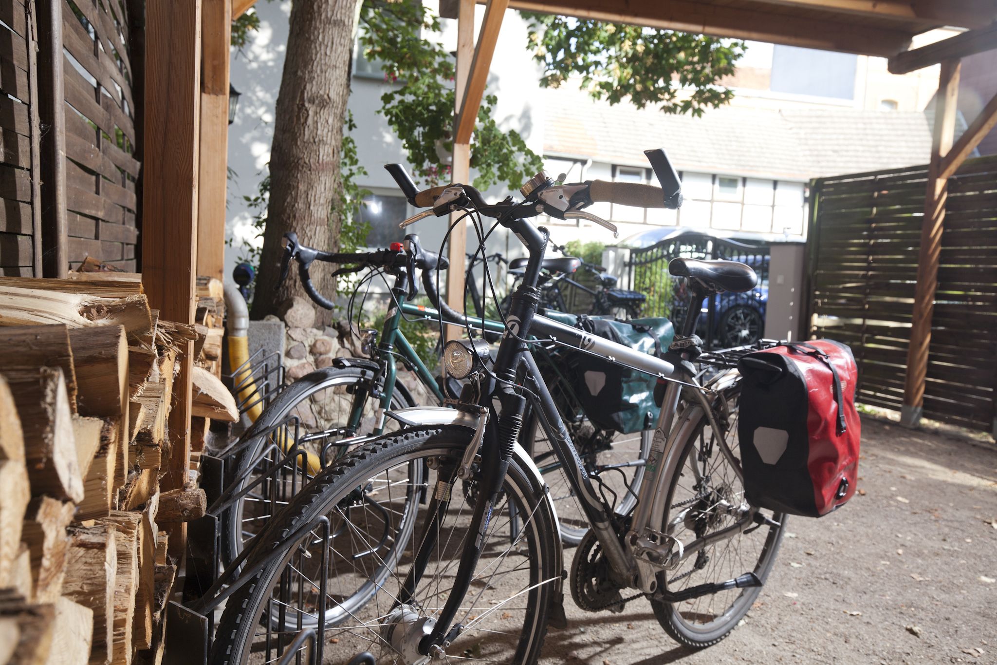 Bicycles parked under a wooden structure with a tree nearby.