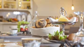 Una mesa con panes y pasteles variados, una tetera y un cuenco pequeño de fruta.