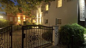 Une courClose, accessible par un chemin pavé de pierres, mène à un bâtiment dont les fenêtres sont illuminées et sur lequel on peut lire l’inscription « ALTIADI GASTHAUS ».