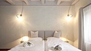 Un lit double avec du linge de lit blanc, deux tables de chevet avec des lampes et une tête de lit de couleur neutre.