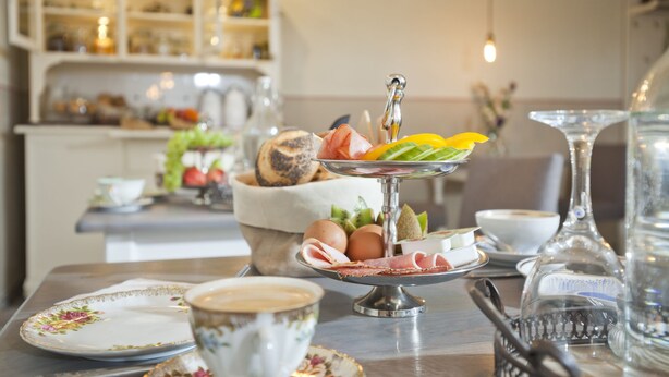 Une table de petit-déjeuner agrémentée d’un présentoir à étages, d’une tasse à café et d’un vase décoratif.