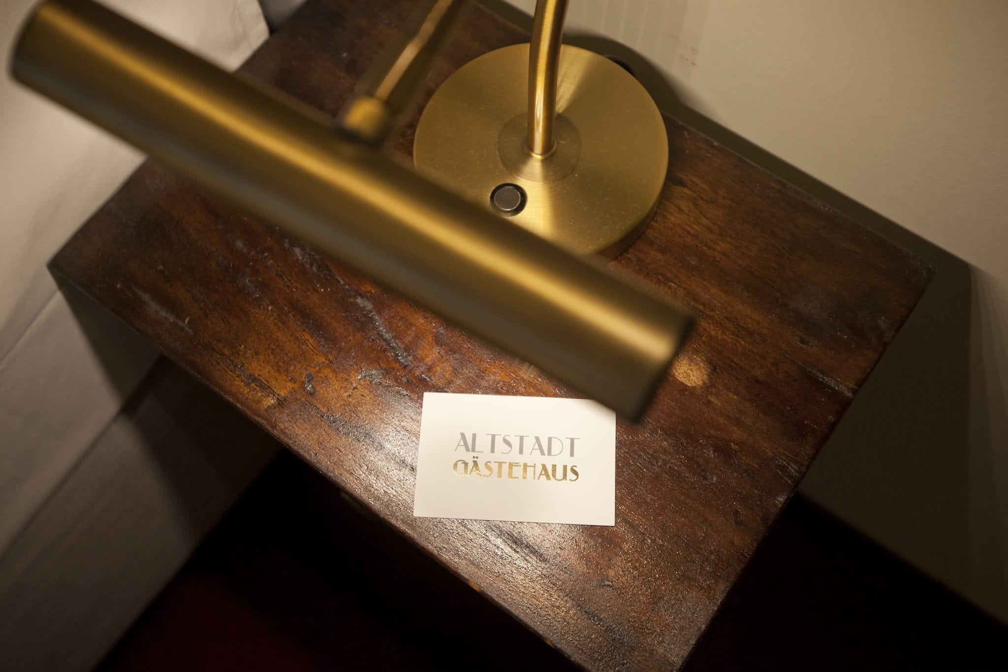 A brass lamp on a wooden table with a sign that reads "ALTSTADT OASTEHAUS".