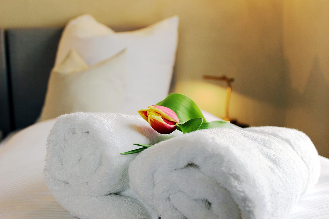 Ein ordentlich bezogenes Bett mit aufgerollten weißen Handtüchern und einer einzelnen Tulpe.