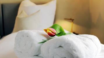 Ein ordentlich bezogenes Bett mit aufgerollten weißen Handtüchern und einer einzelnen Tulpe.
