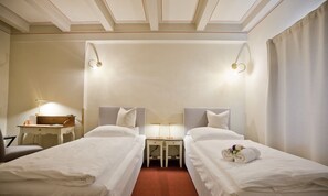 Een hotelkamer met twee enkele bedden, een bureau met lamp en een kleine tafel met lamp.
