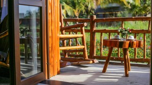 A wooden deck with a table and chairs, a glass door, and a view of greenery. - Can Tho Ecolodge (Can Tho)