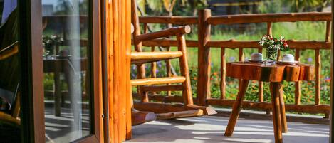 A wooden deck with a table and chairs, a glass door, and a view of greenery.