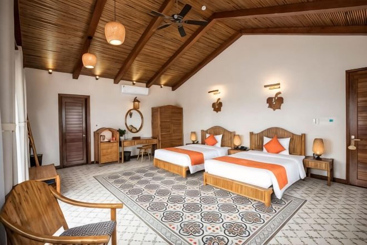 A room with two beds, a desk, a chair, and a ceiling fan.
