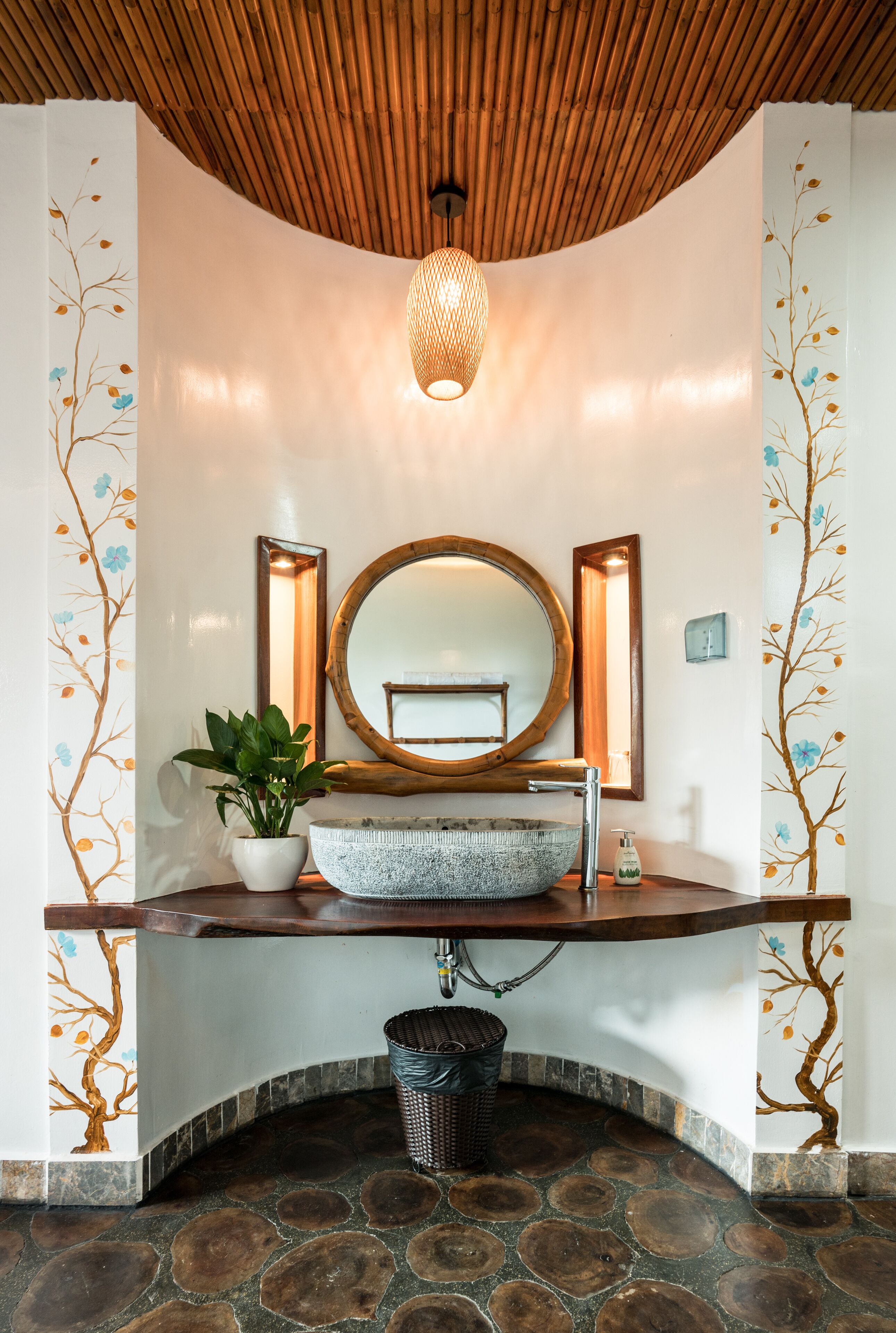 A bathroom with a wooden ceiling, a round mirror, a stone sink, and a potted plant.