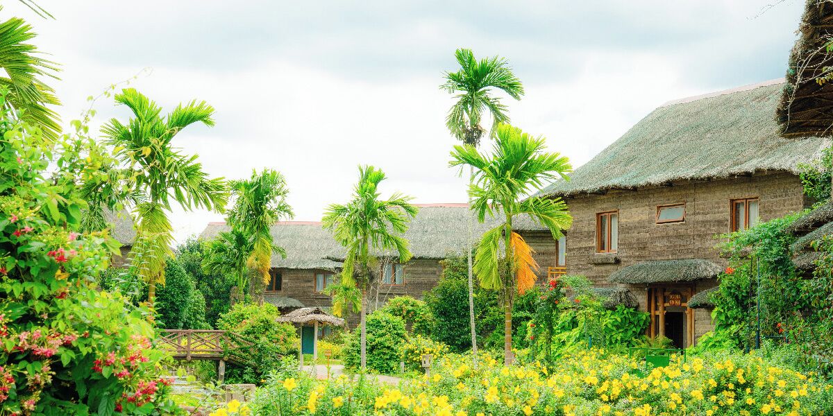 A traditional village with thatched-roof houses surrounded by lush greenery and flowering plants.