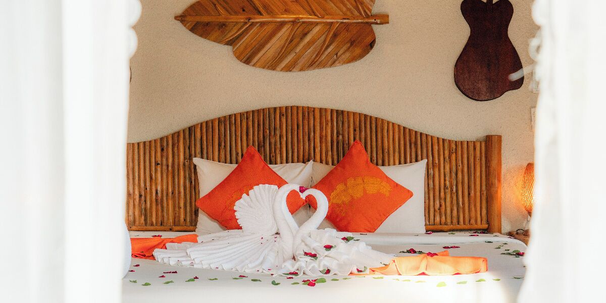 Una cama con cabecera de madera, almohadas anaranjadas y una decoración de cisne blanco.