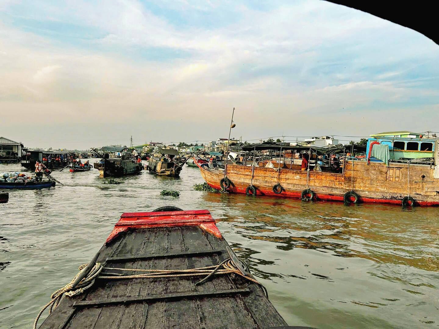 A river with several boats docked, a wooden boat in the foreground, and buildings in the background.
