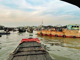 A river with several boats docked, a wooden boat in the foreground, and buildings in the background.