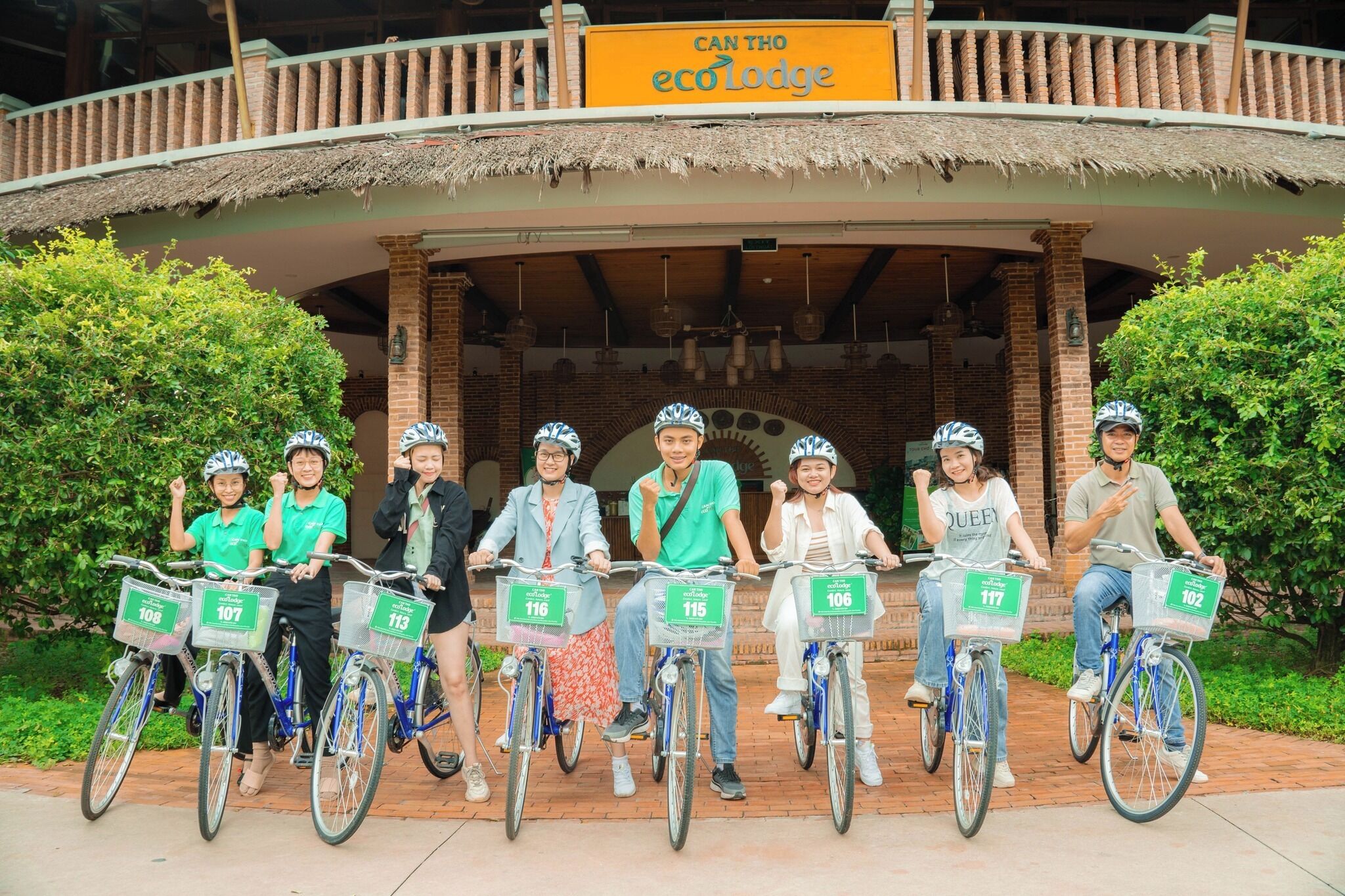 A group of people on bicycles in front of a building with a sign that reads "CAN THO ecoLodge".