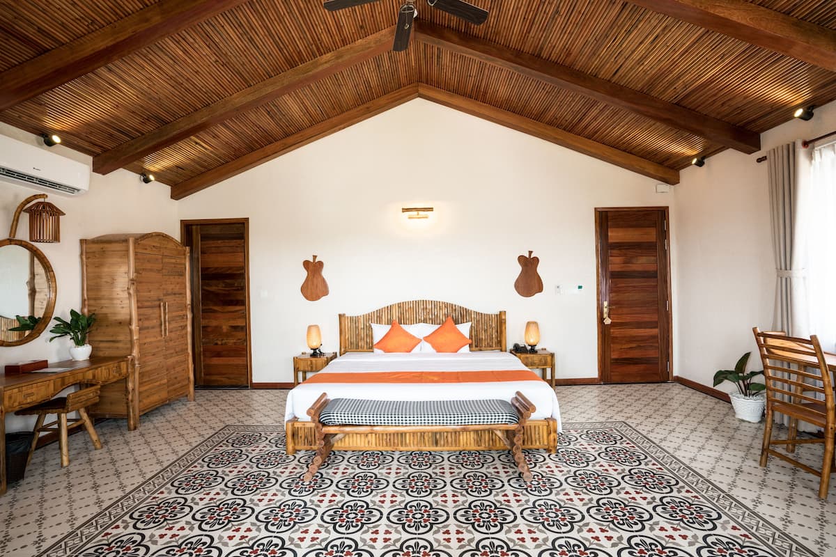 Une chambre avec un haut plafond en bois, un grand lit avec une literie orange, un bureau en bois et un sol à motifs.