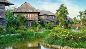 A traditional wooden house with a thatched roof, surrounded by lush greenery and a small pond. - Can Tho Ecolodge (Can Tho)