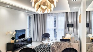 A modern living room with a black sofa, a round coffee table, a TV, and a decorative plant. - Angielska Grobla City Center & Parking by Downtown Apartments (Gdansk)