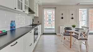 A modern kitchen with white cabinets, a black countertop, and a dining area with a white table and chairs. - Angielska Grobla City Center & Parking by Downtown Apartments (Gdansk)