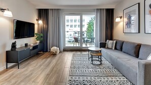 A modern living room with a grey sofa, a black entertainment unit, a patterned rug, and a view through a glass door to an outdoor area with a table and chairs. - Angielska Grobla City Center & Parking by Downtown Apartments (Gdansk)