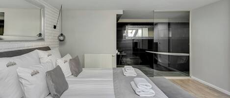A modern bedroom with a large bed, a bench, and a glass shower area.