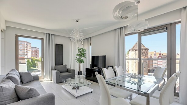 Een moderne woonkamer met een glazen salontafel, een grijze bank en een eethoek met witte stoelen.