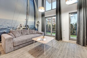 Uma sala de estar moderna com uma janela grande, um sofá, uma mesa de centro e um mural de um veleiro na parede.